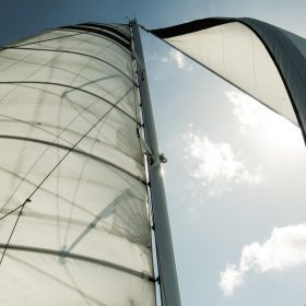 Looking up at white canvas sailboat sails in the wind